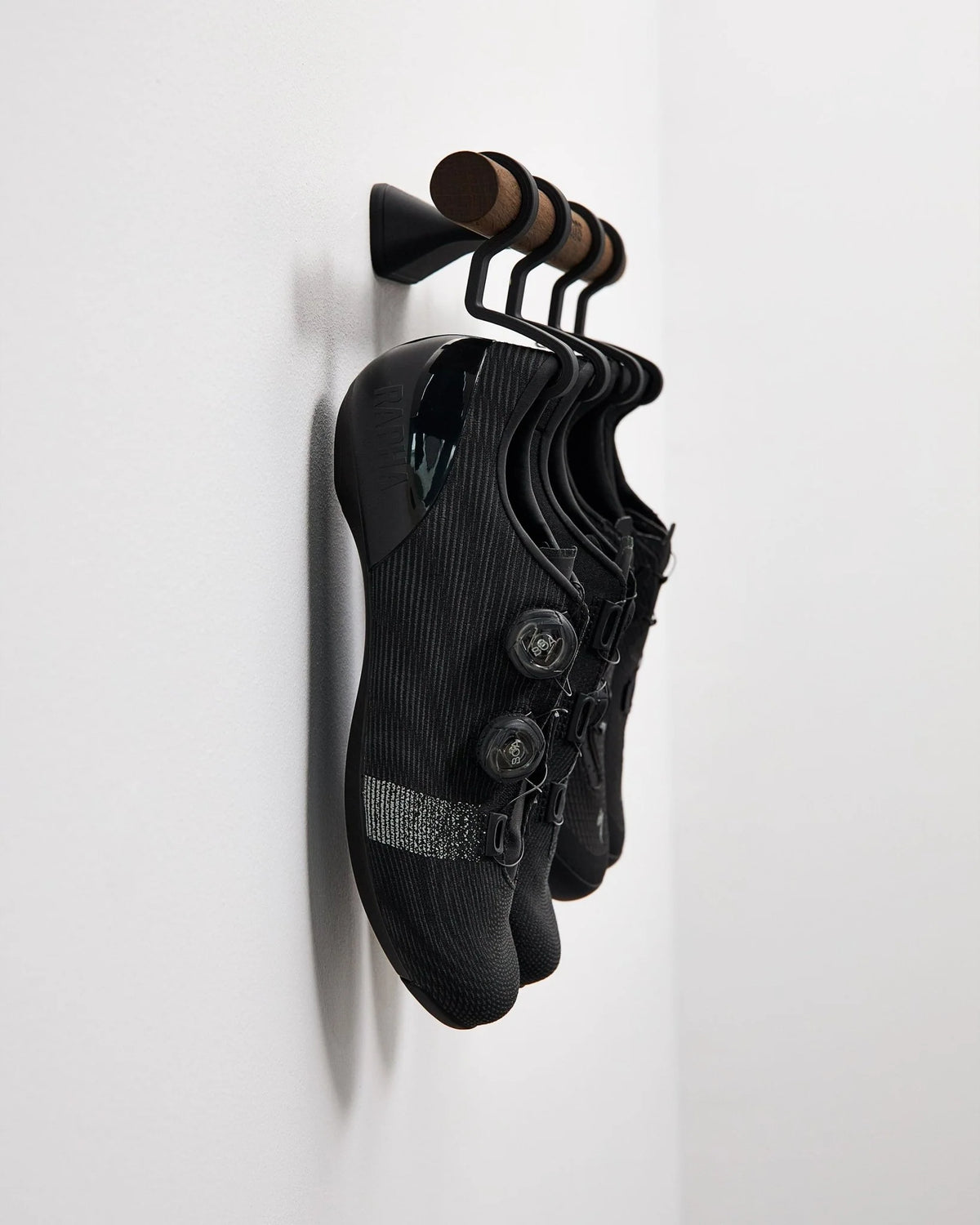 スモークドオークの Short Bar C に黒いサイクルシューズ2ペアを掛けた側面クローズアップ